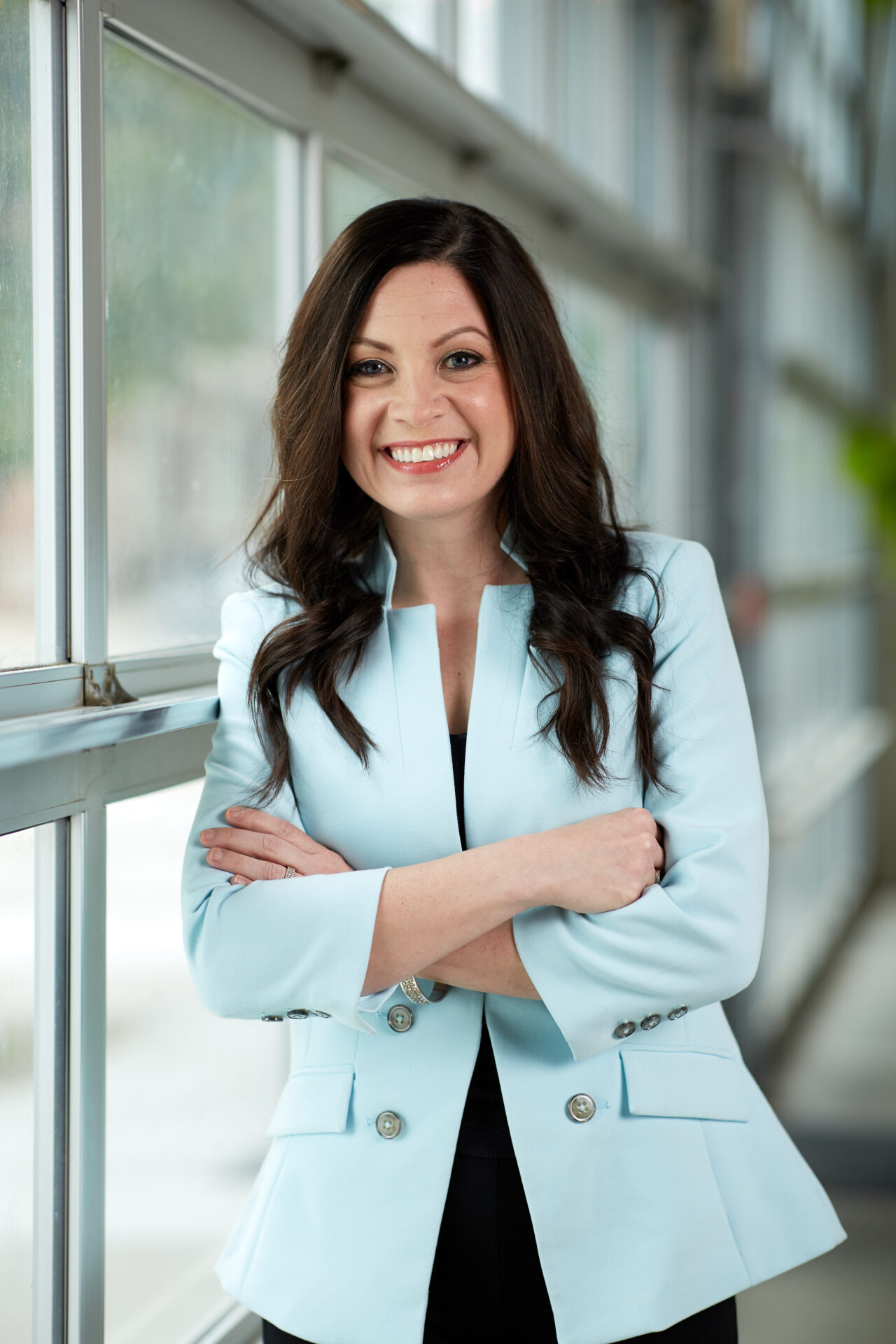 A woman standing in front of a window with her arms crossed.